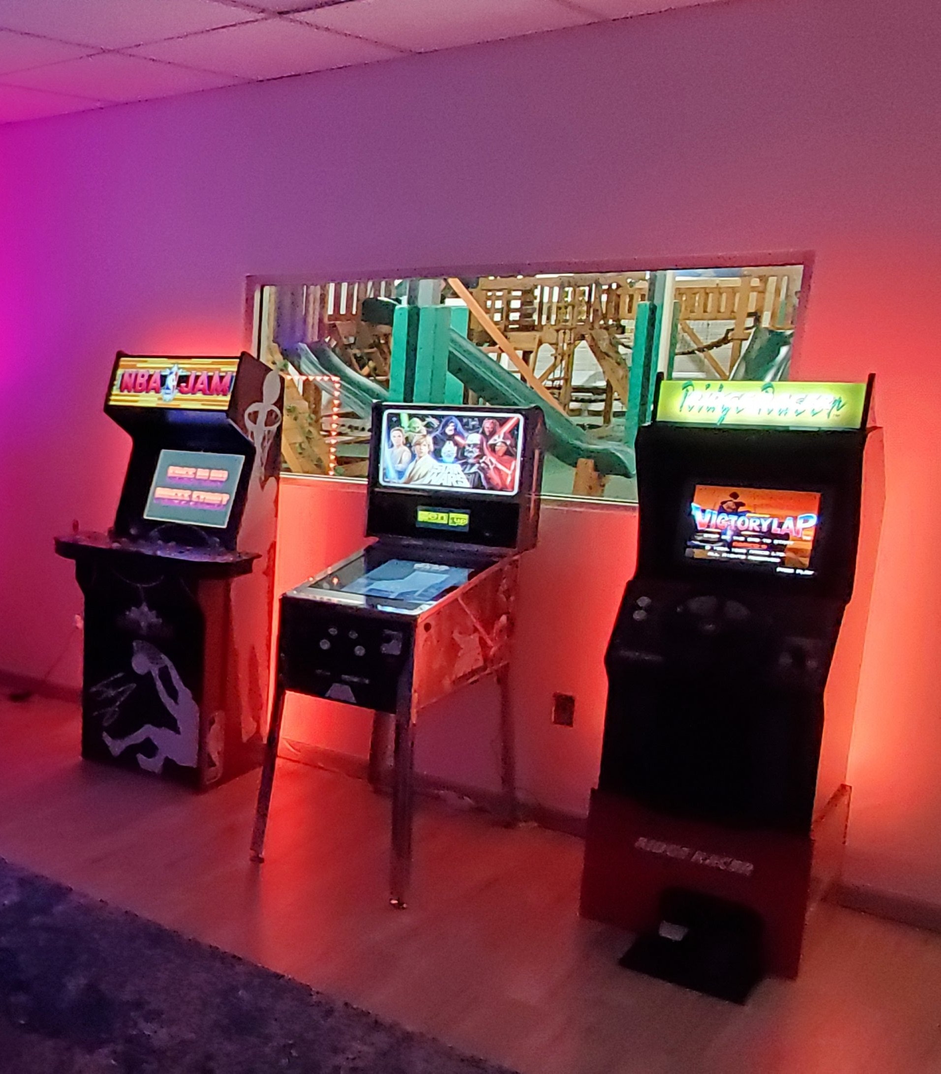Arcade machines and a pinball machine in the mini arcade, with swing sets visible through the window