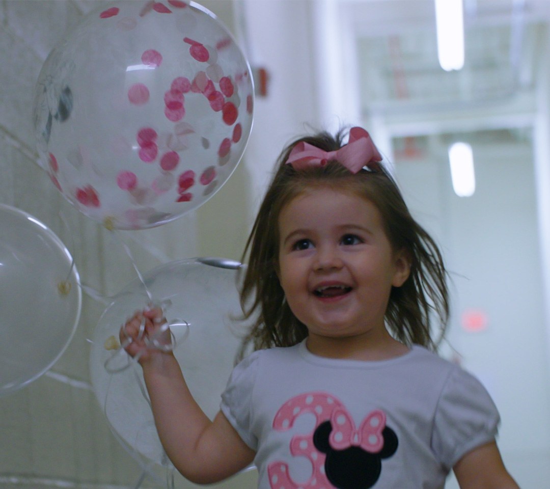 A smiling toddler holding clear confetti balloons at the showroom