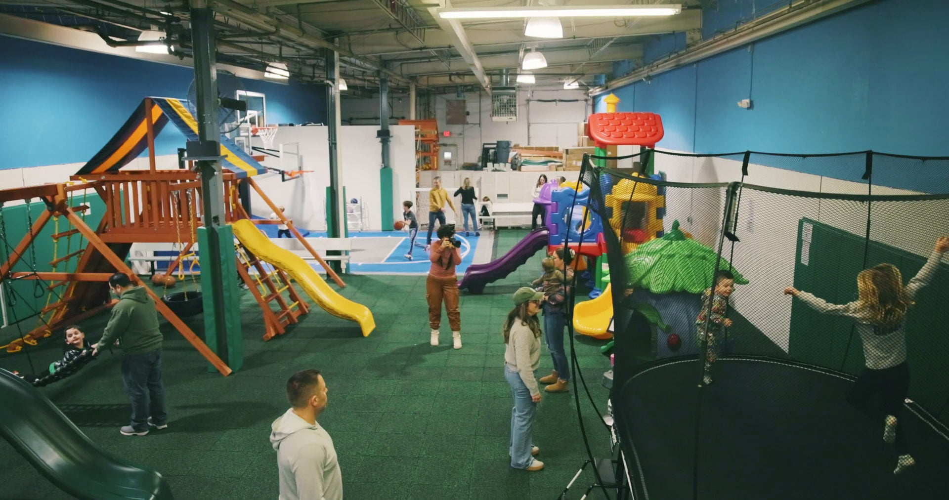 Kids playing on swing sets, a trampoline and the basketball court inside the NJ Swingsets & Playgrounds showroom in Midland Park