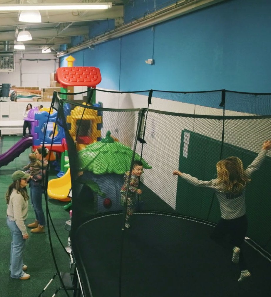 Kids jumping on an enclosed trampoline next to the toddler play structures while parents watch