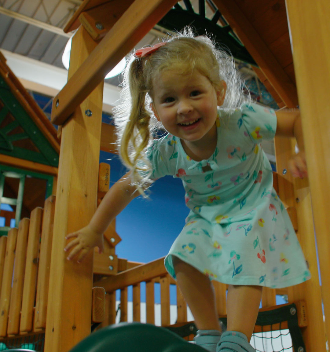 A little girl climbing through the fort of a wooden swing set