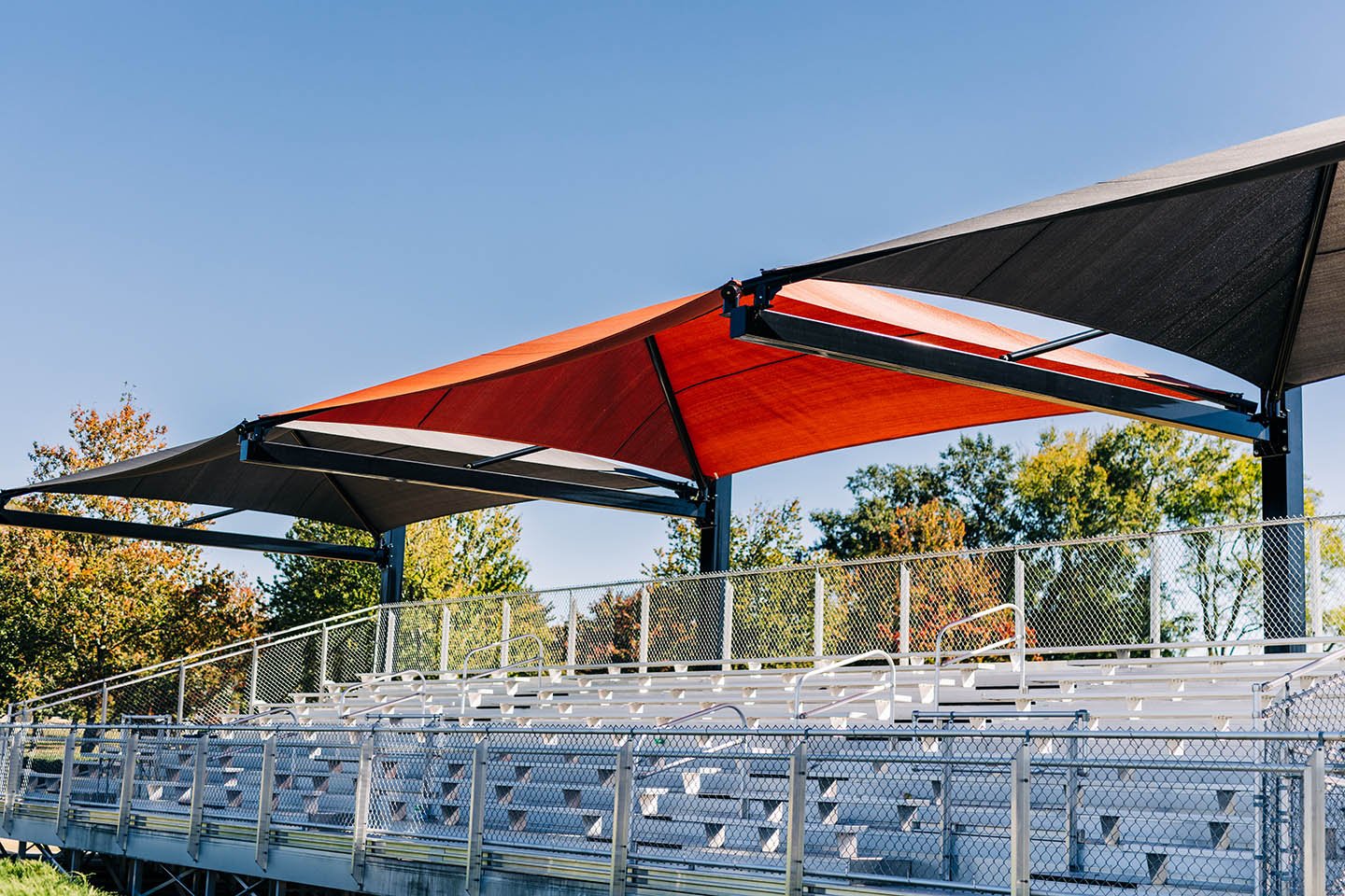Orange and grey suspended cantilever shade over aluminum bleachers