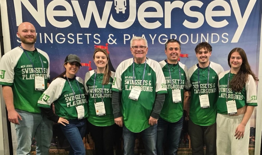 Seven members of the NJ Swingsets & Playgrounds team in green team jerseys in front of the company banner