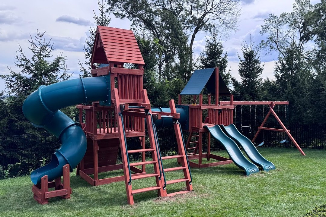 Cedar Playground One swing set with a green spiral tube slide, two towers, two wave slides and a swing beam in a backyard lawn