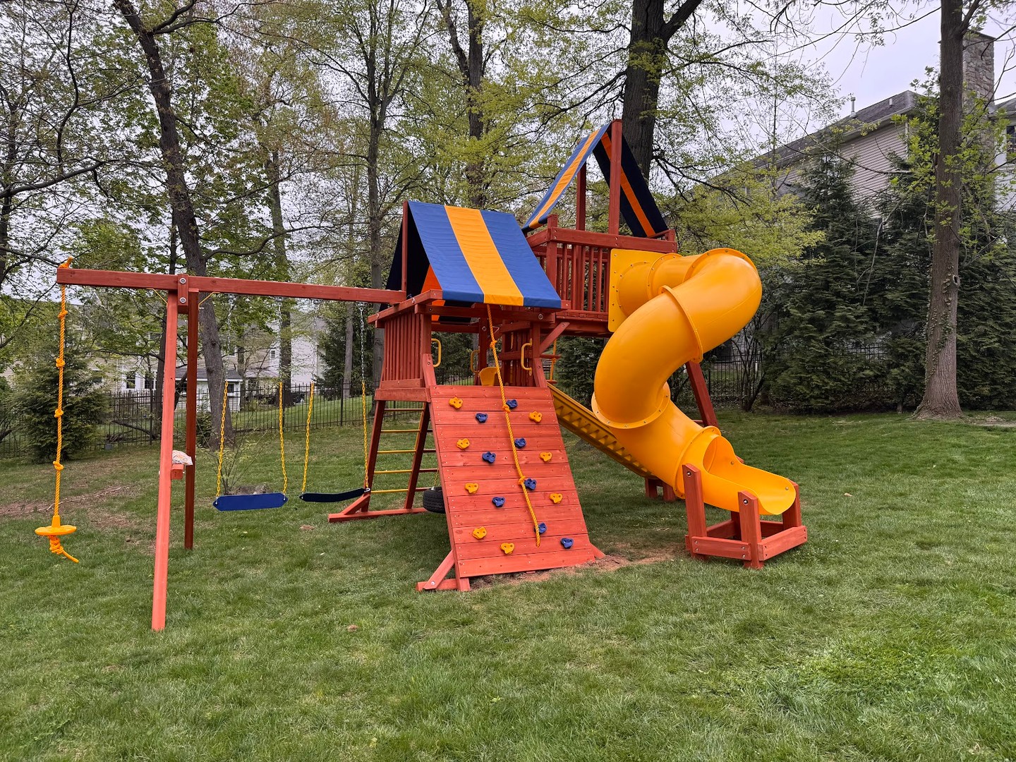 Wooden swing set with a yellow tube slide and a striped canopy roof