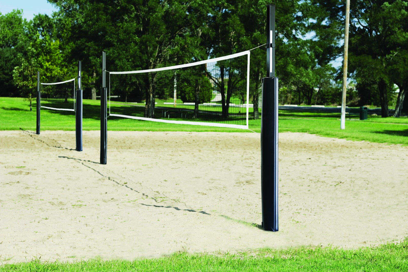 Padded volleyball posts and net on a sand court in a park