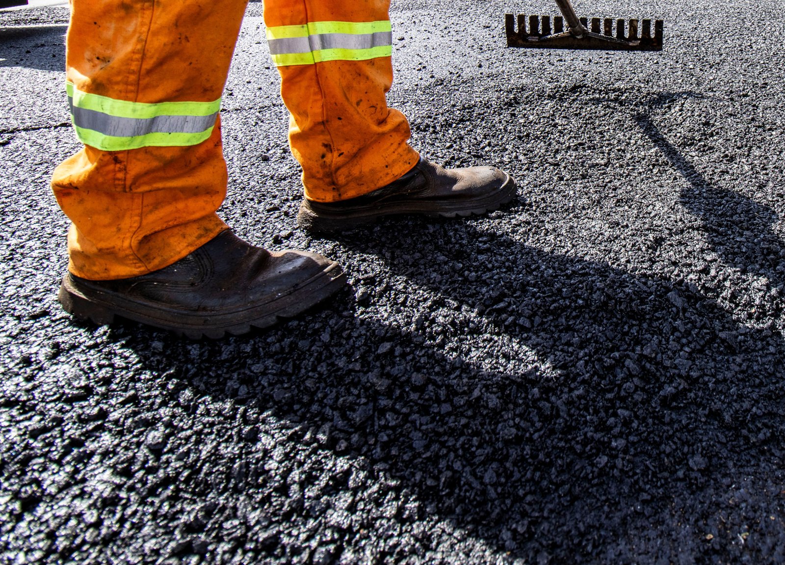 Worker raking fresh hot asphalt during paving