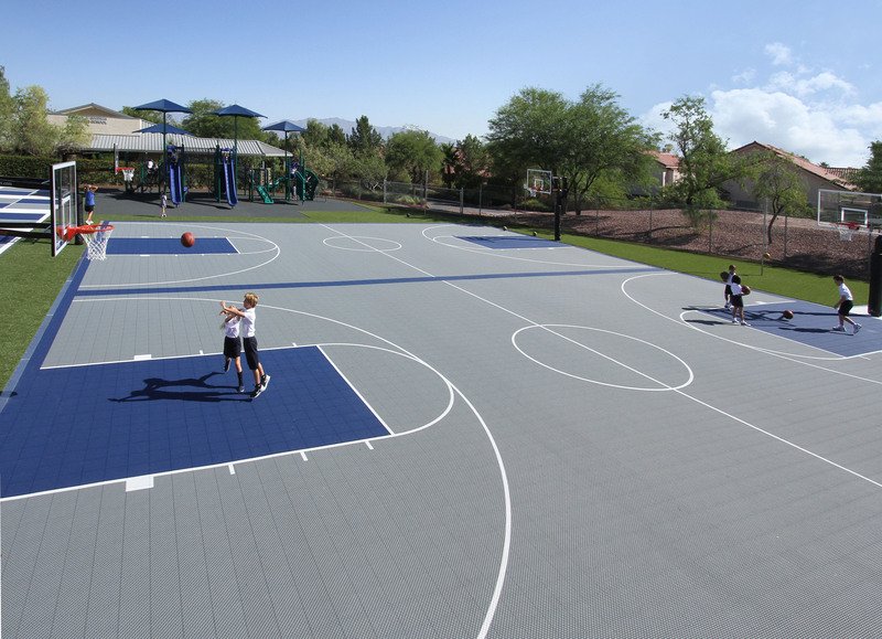 Kids playing basketball on a grey and blue sports court tile court in a park
