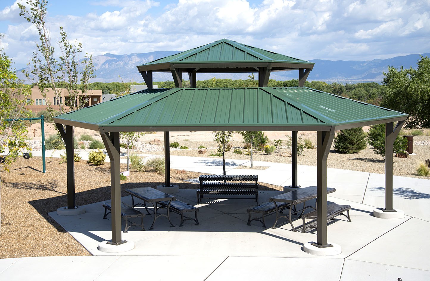 Two-tier hexagon SRP steel shelter with a green metal roof over picnic tables on a concrete pad