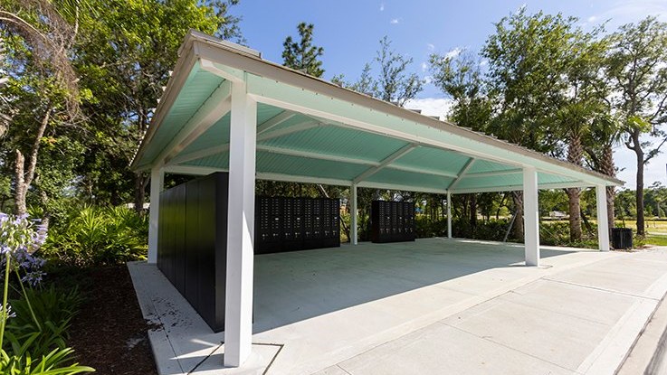 Rectangular hip-end steel shelter with white columns and a pale green ceiling over a concrete pad lined with mailboxes