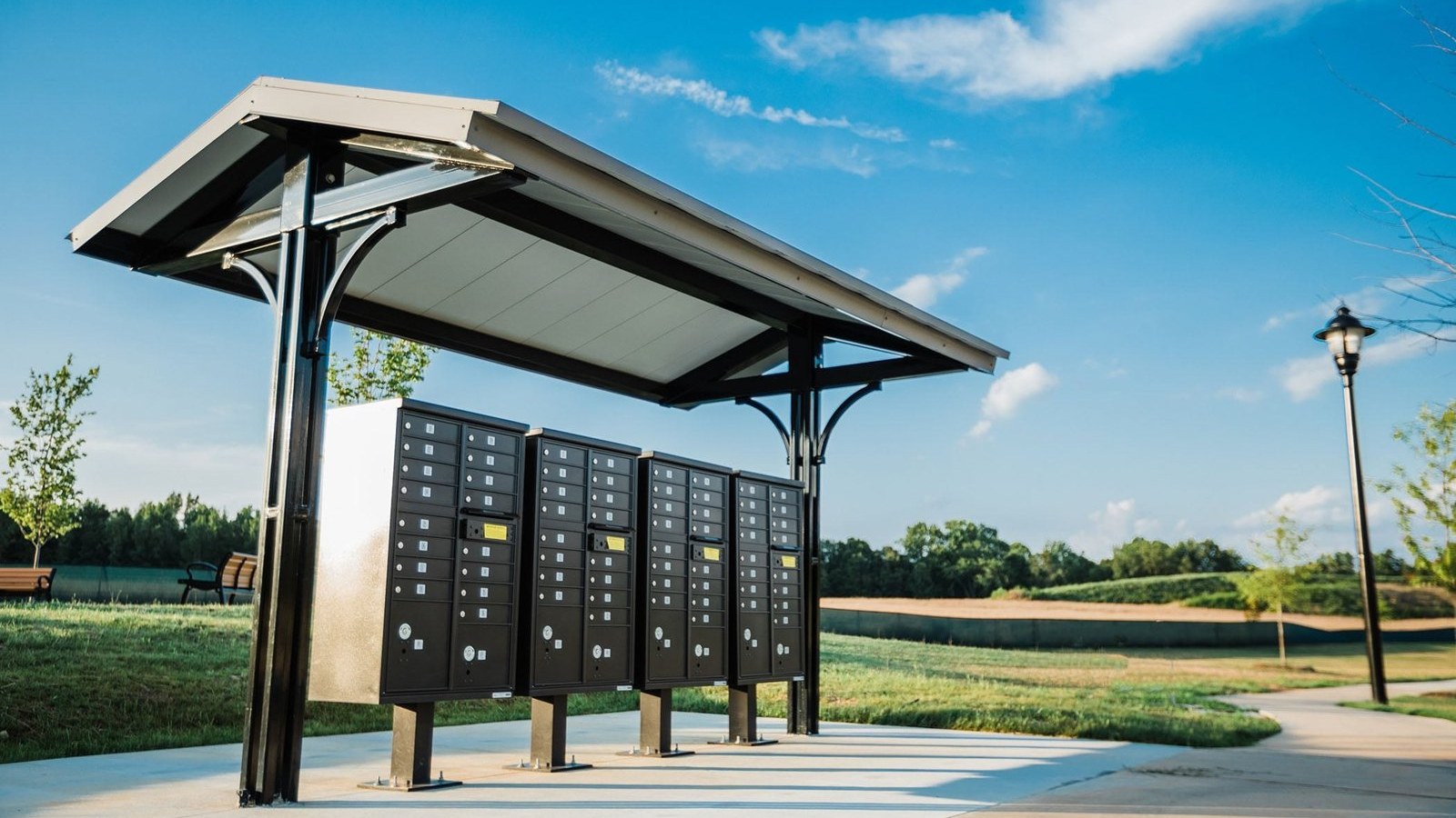 Small steel shelter with a shallow gable metal roof over a row of cluster mailboxes on a concrete pad
